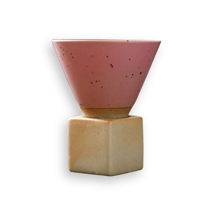 Pink, speckled ceramic cone coffee cup on a square wooden base.