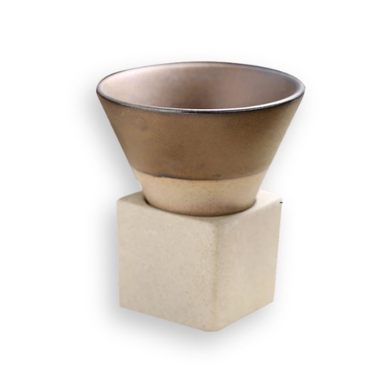 A brown ceramic coffee cup with a light rim, resting on a square light brown base.