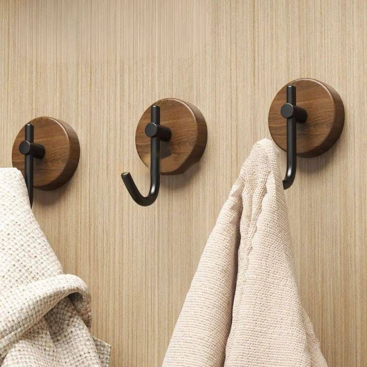 Three wooden coat hooks on a wooden wall, two with towels hanging.