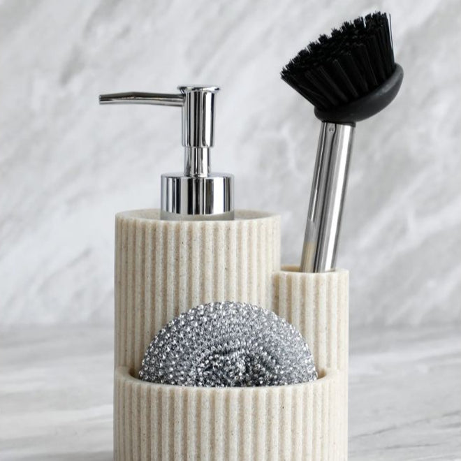 Beige kitchen detergent dispenser holding a metal scrubber and dish brush on marble countertop.