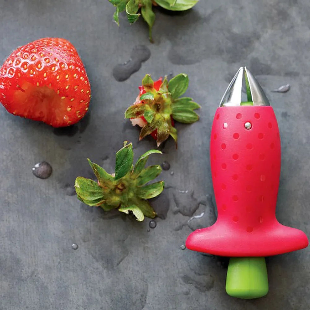Red fruit corer placed beside strawberries on a dark surface.
