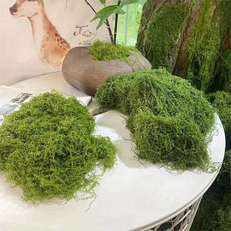 Bundles of fake moss displayed on a white table and wooden planter.