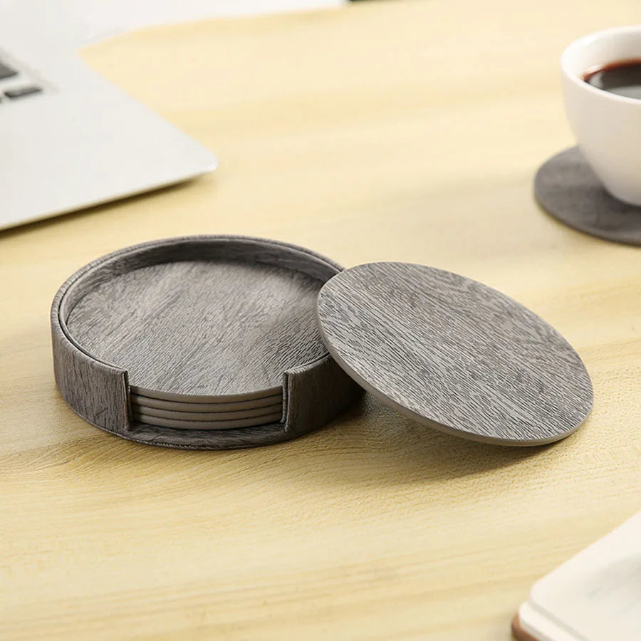 Set of 6 grey leather coasters with wood grain texture in holder, one removed.