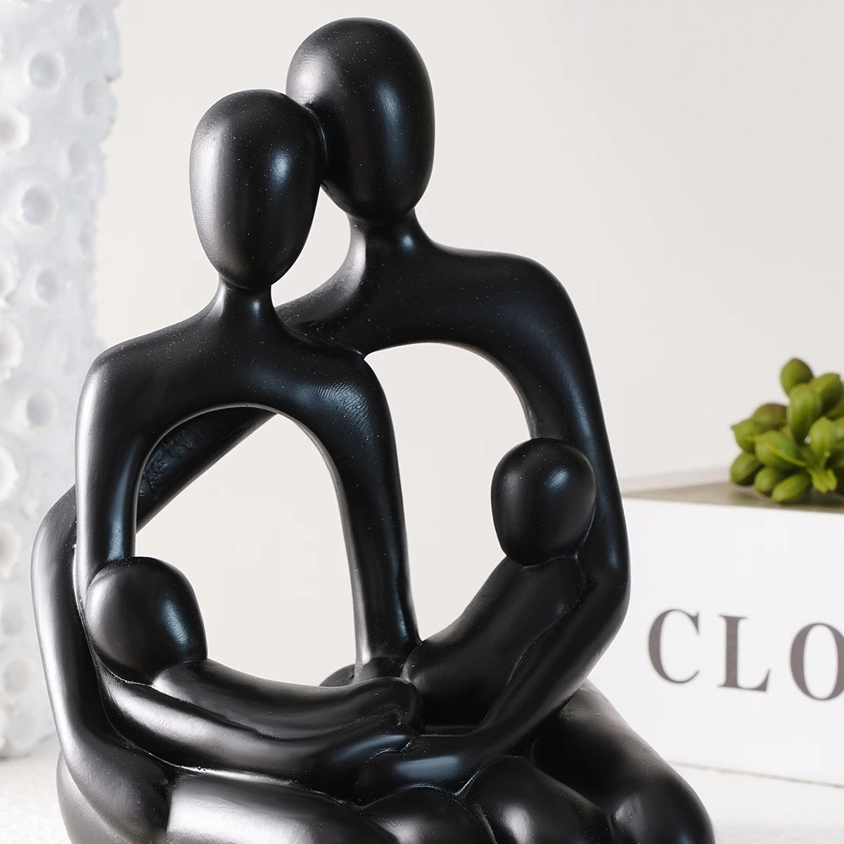 Black hugging couple desk statue next to greenery on a white ledge.