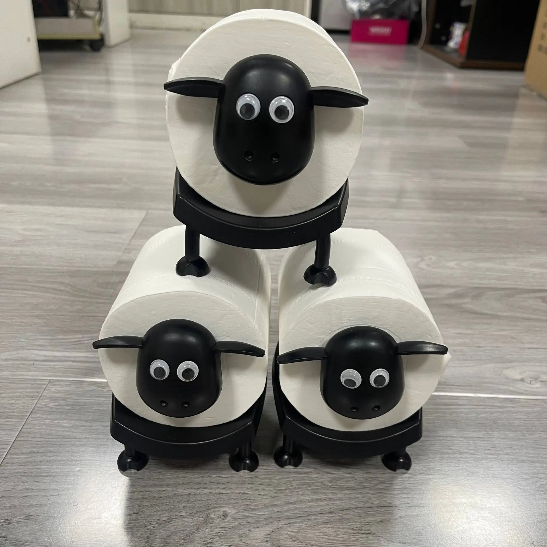 A wall-mounted black toilet roll holder with a top shelf, holding a potted plant.