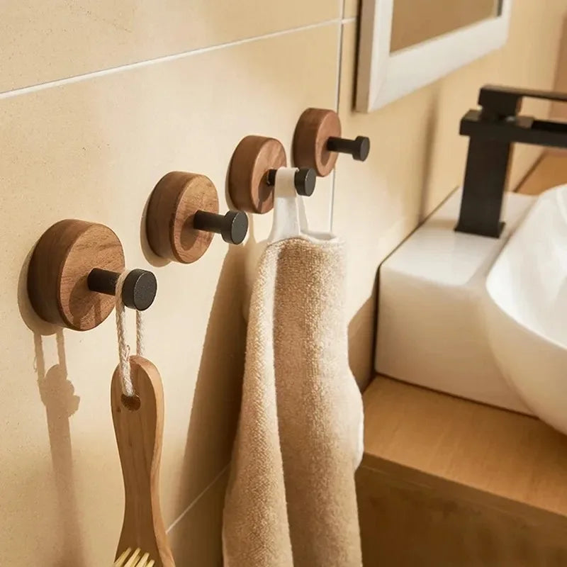 Four round wood hooks with black pegs, two holding towels and one a brush.
