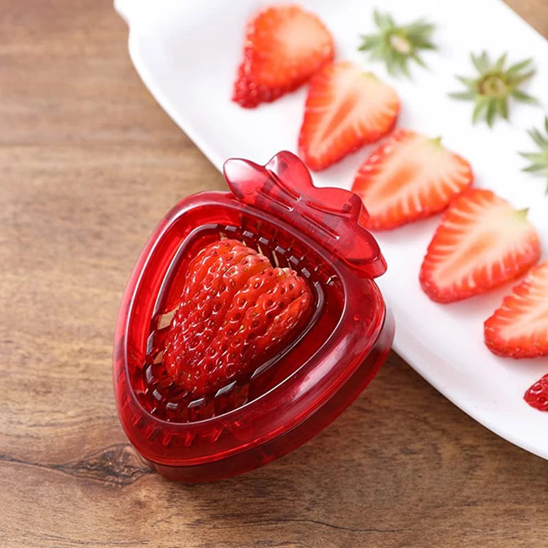 A red, heart-shaped strawberry slicer next to sliced strawberries on a white plate.