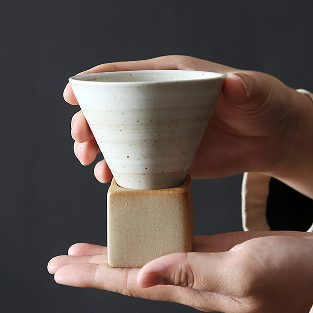 Hands holding a white ceramic coffee cup on a wooden stand.