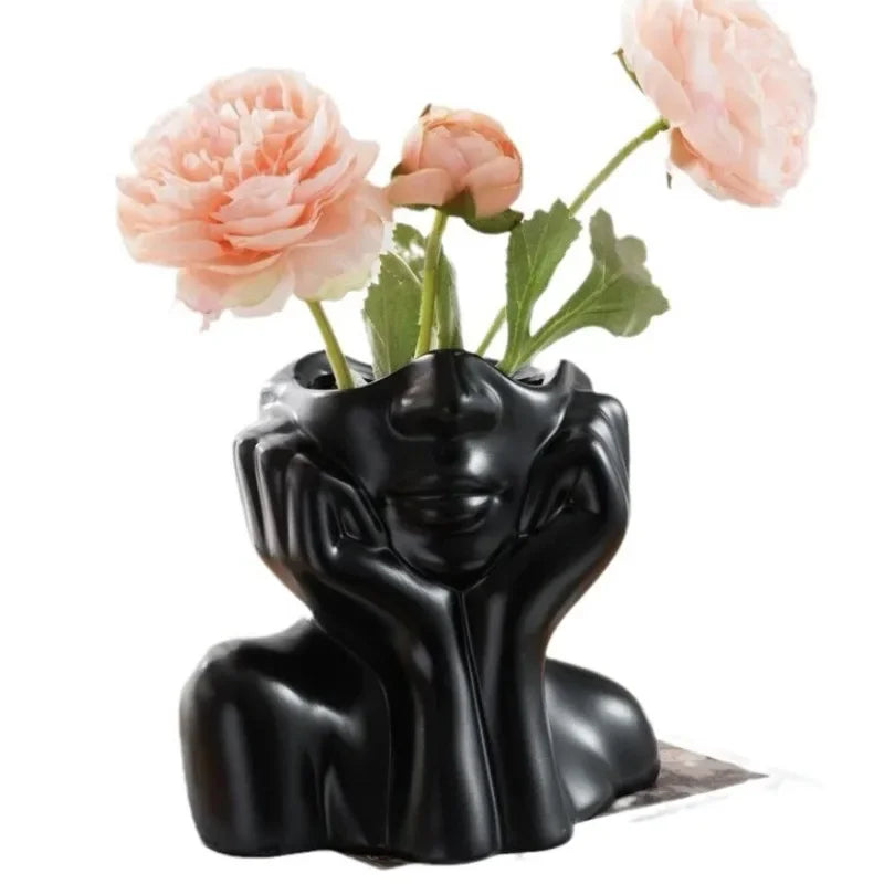 Black body shape vase with pink flowers on a white table.