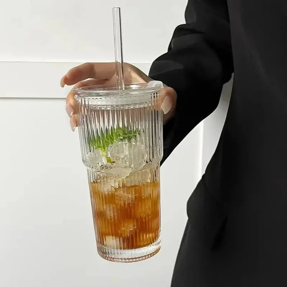 Hand holding a glass cup with lid and iced tea.