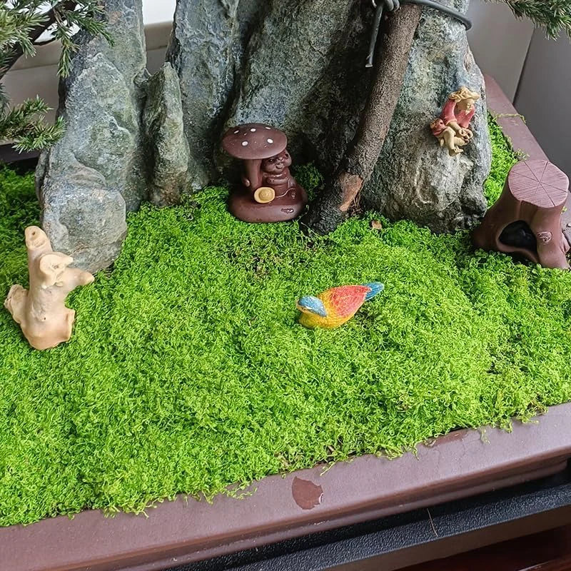Miniature garden scene with figurines and fake moss ground cover.