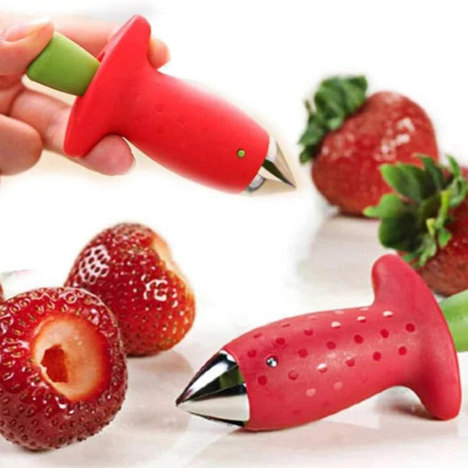 Red fruit corer removing stem from a strawberry on a table.