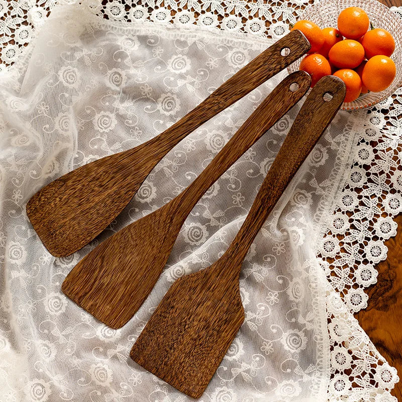Three pieces of wooden kitchenware displayed next to decorative fruits.