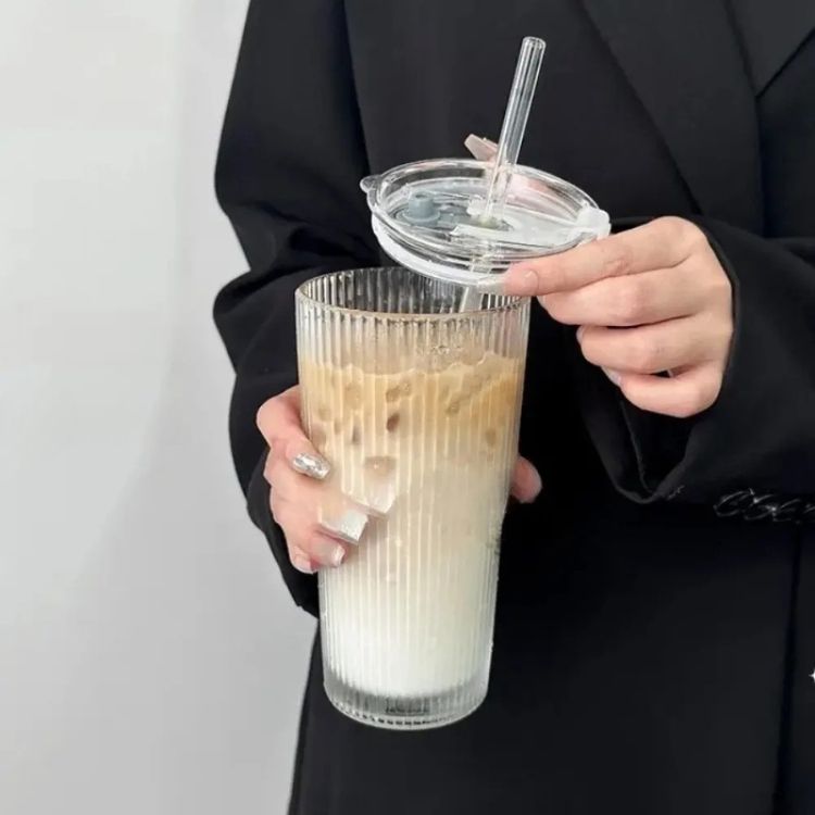 Person lifting lid from glass cup with milk tea.