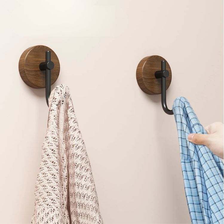 Two wooden coat hooks with black metal arms holding shirts.