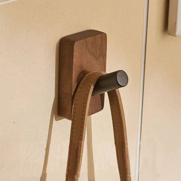 A rectangular wood hook with a black peg holding a brown leather strap.