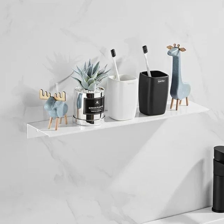 White bathroom with black floating wall shelf displaying decorative items.