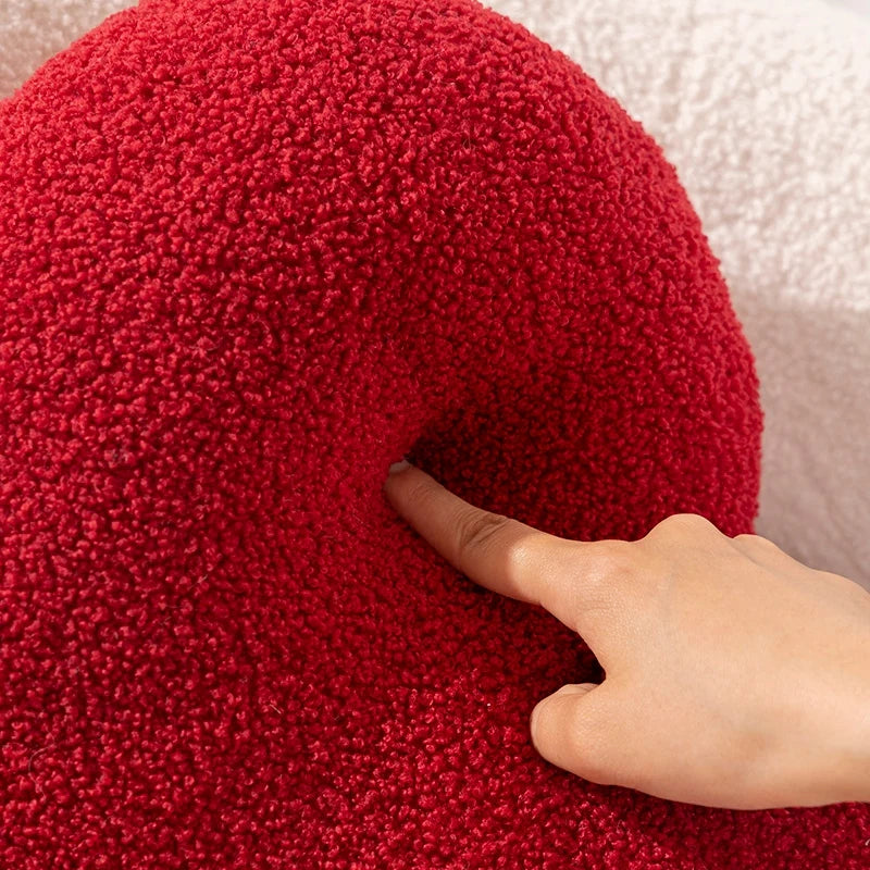 A close-up of a red Heart Shape Throw Pillow being gently pressed by a finger, showing its soft and plush texture.