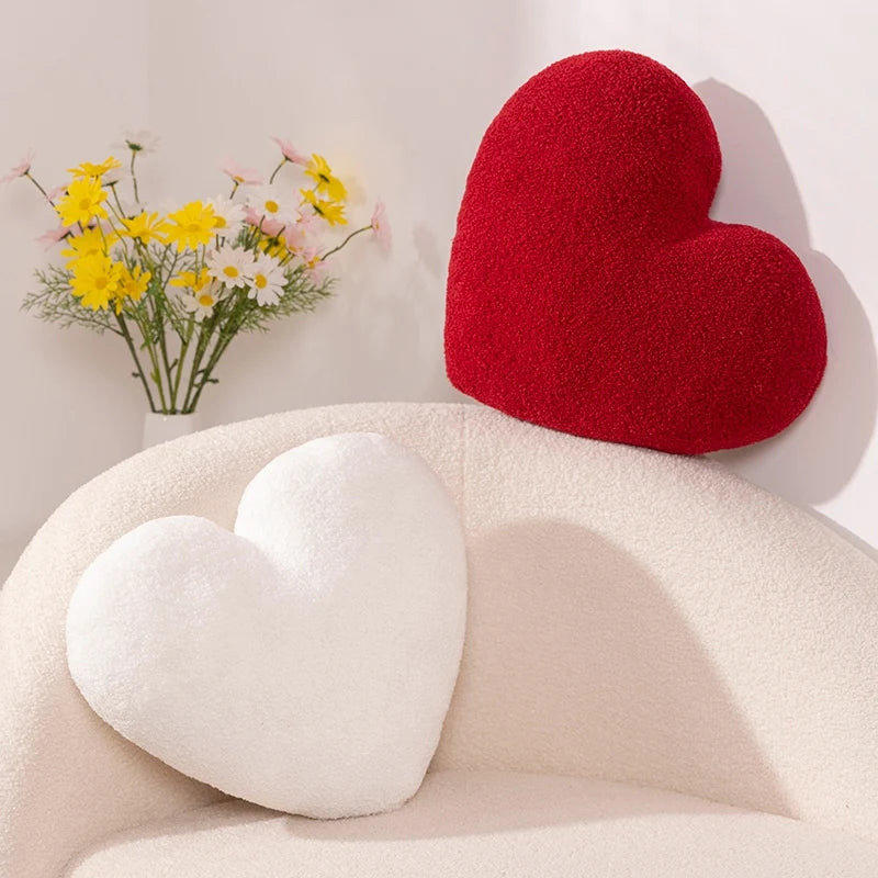 Red and white Heart Shape Throw Pillows on a cream-colored chair with a vase of yellow and white flowers in the background.