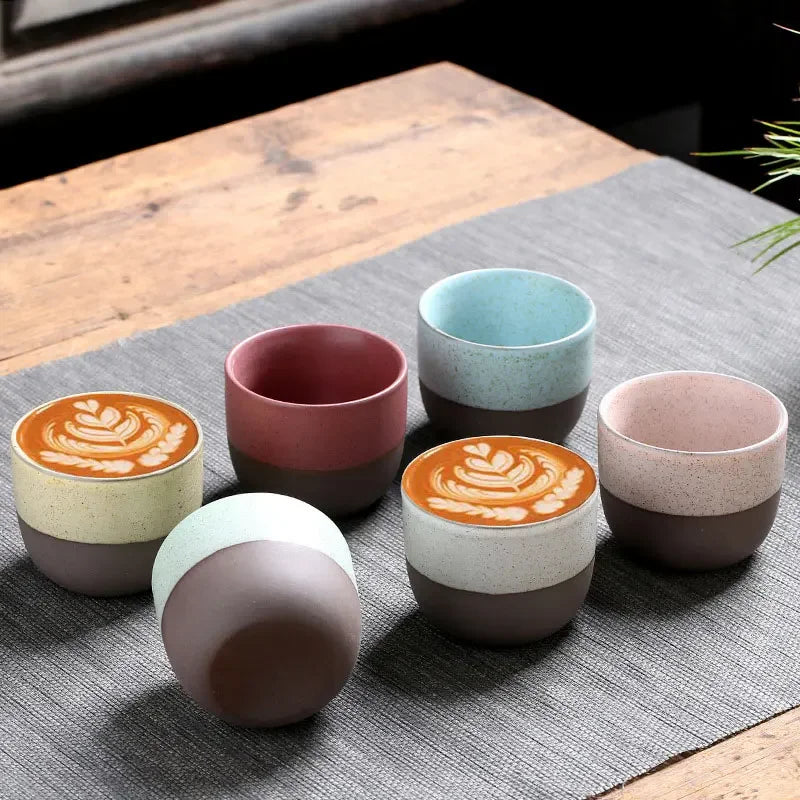 A set of colorful Kung Fu Teacups on a gray placemat, with some filled with latte art and others empty, showcasing a modern ceramic design.