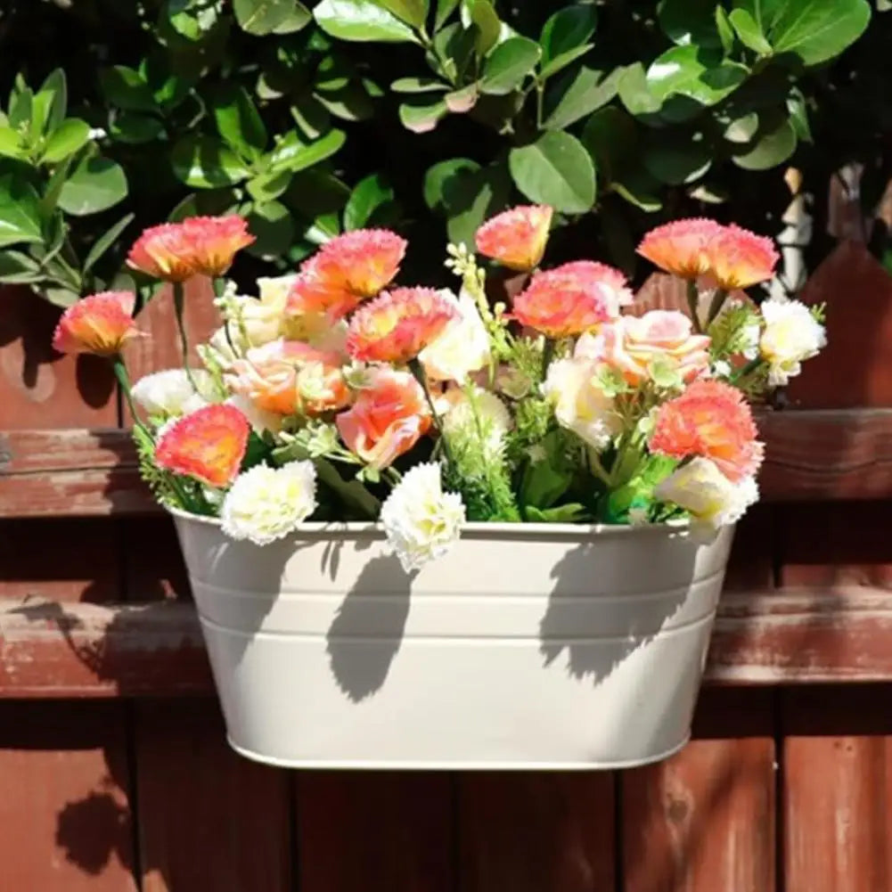 White hanging flower pot with pink and orange blooms on a wooden railing.