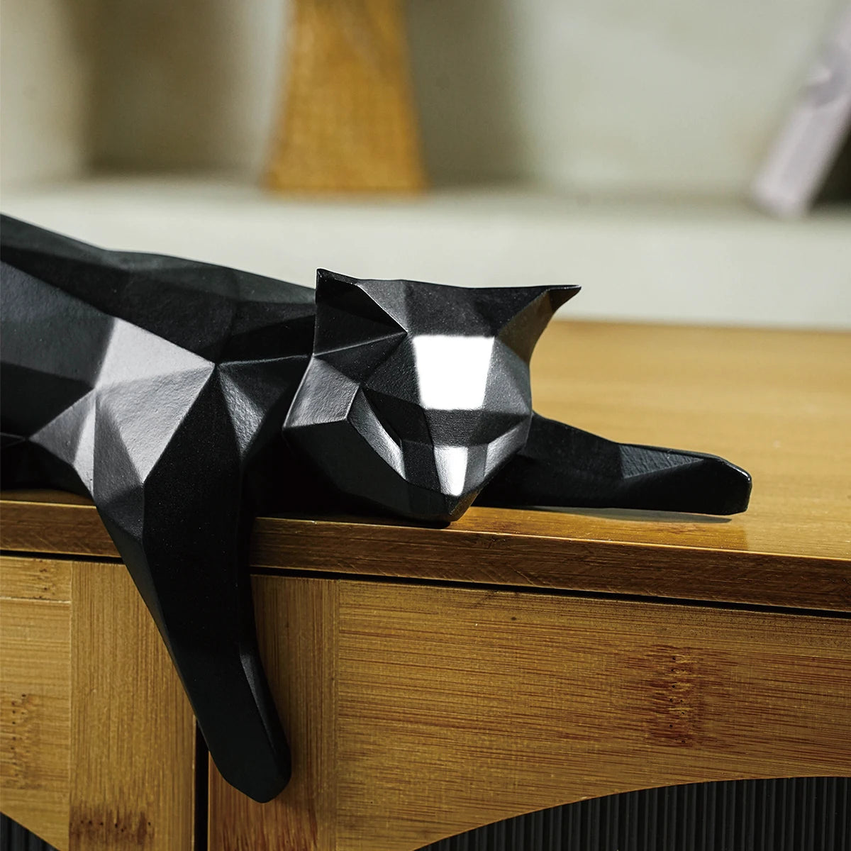 Black cat geometric decor sculpture resting on table edge.