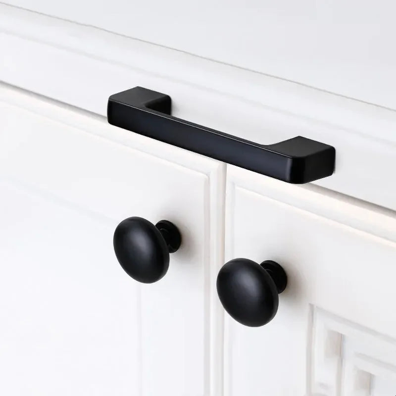 Close-up of black kitchen cabinet knob mounted on a white cabinet door.