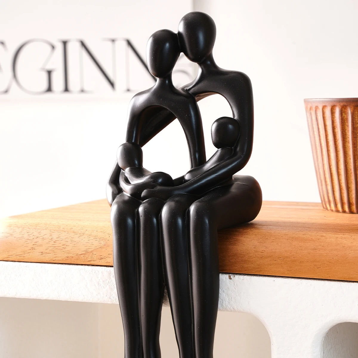 Black couple hugging desk statue displayed beside a book and a plant.