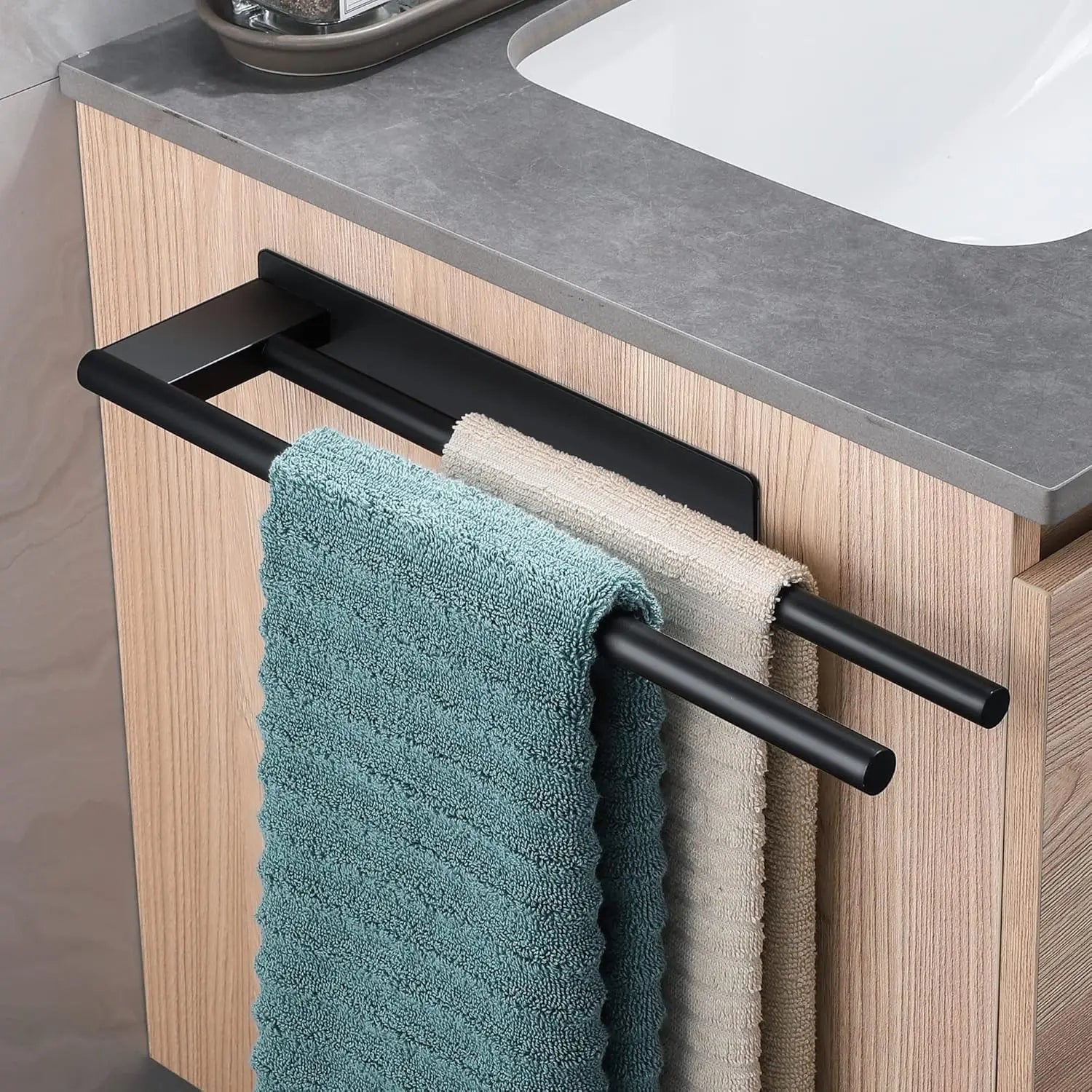 Black adhesive towel bar mounted on a cabinet door, holding two hanging towels.