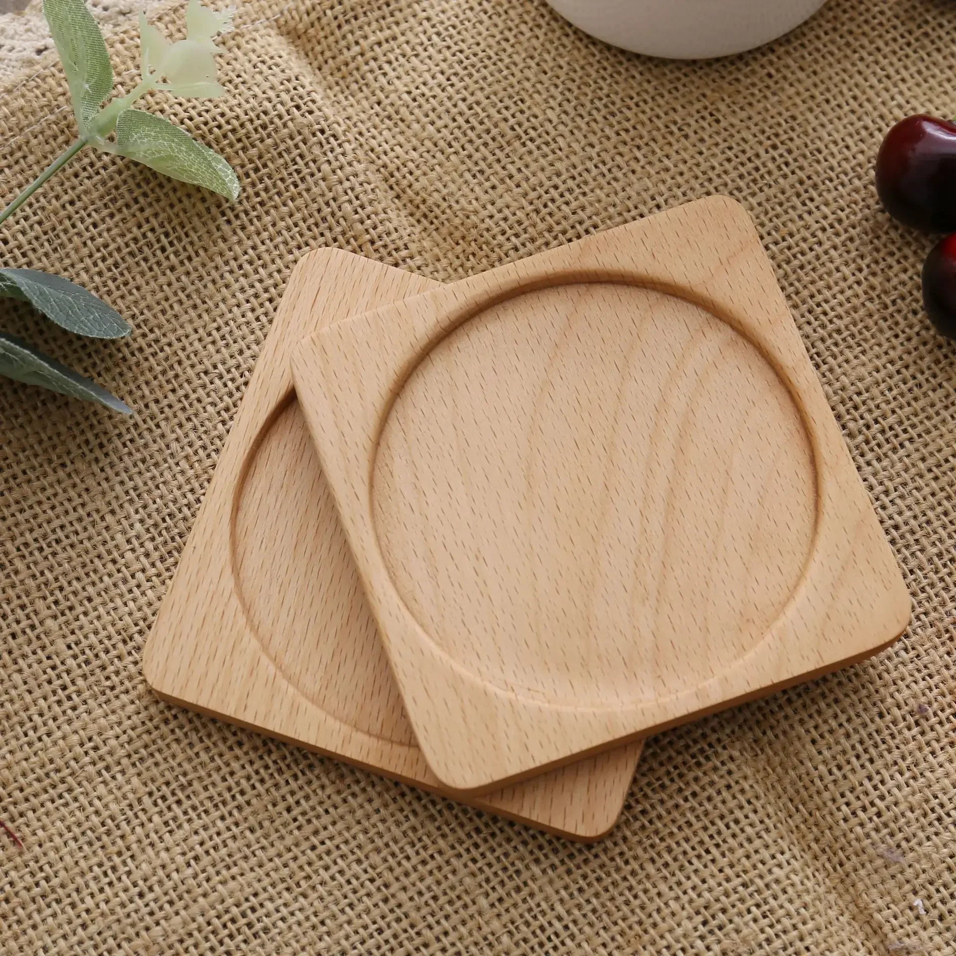 Two light square wooden coasters with circular grooves placed on a textured fabric.