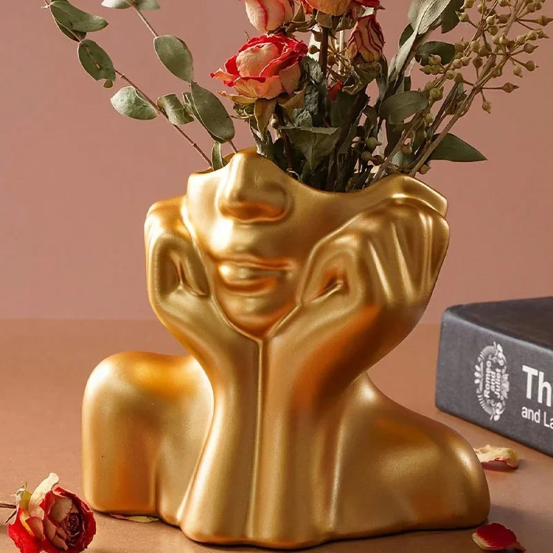 Gold body shape vase holding green and red floral arrangement.