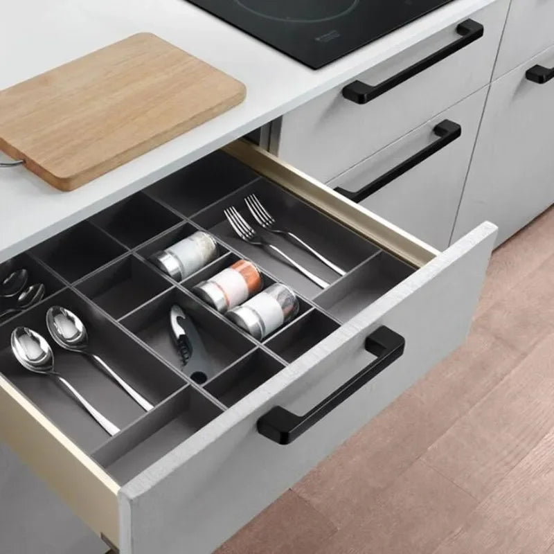 Kitchen drawer pulled open displaying cutlery with black kitchen cabinet knobs.