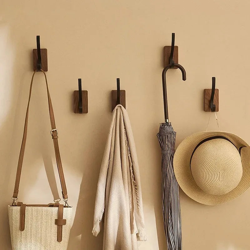 Four wood hooks with black pegs on a wall, holding a bag, a scarf, an umbrella, and a hat.