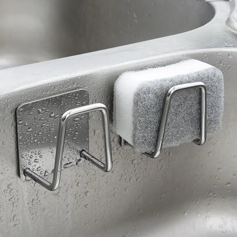 Stainless steel sink sponge rack mounted on the edge of a wet sink, holding a cleaning sponge.