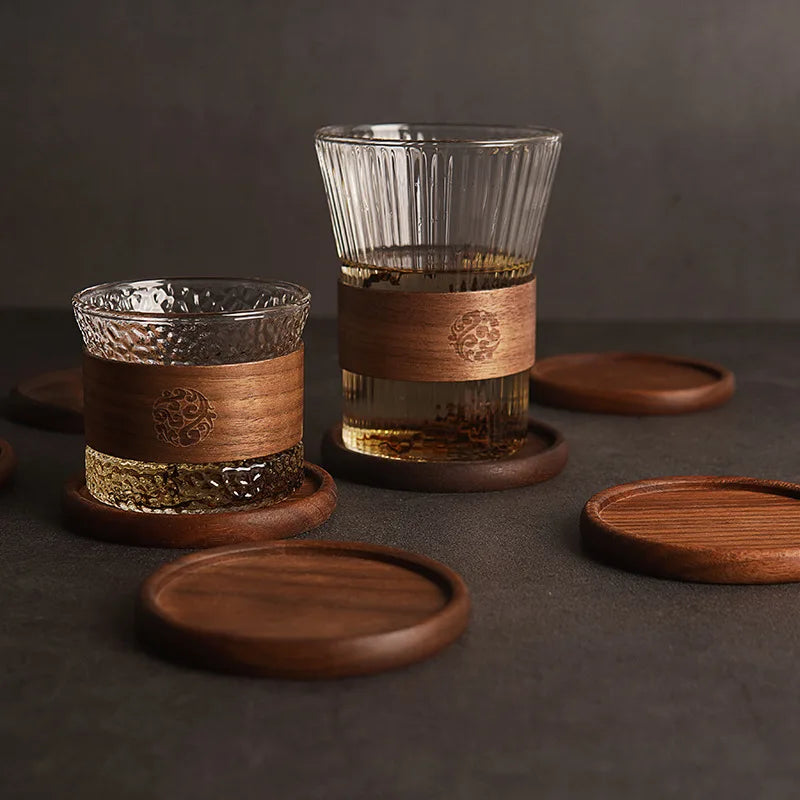 Dark round wooden coasters with short glasses filled with drinks on a black surface.