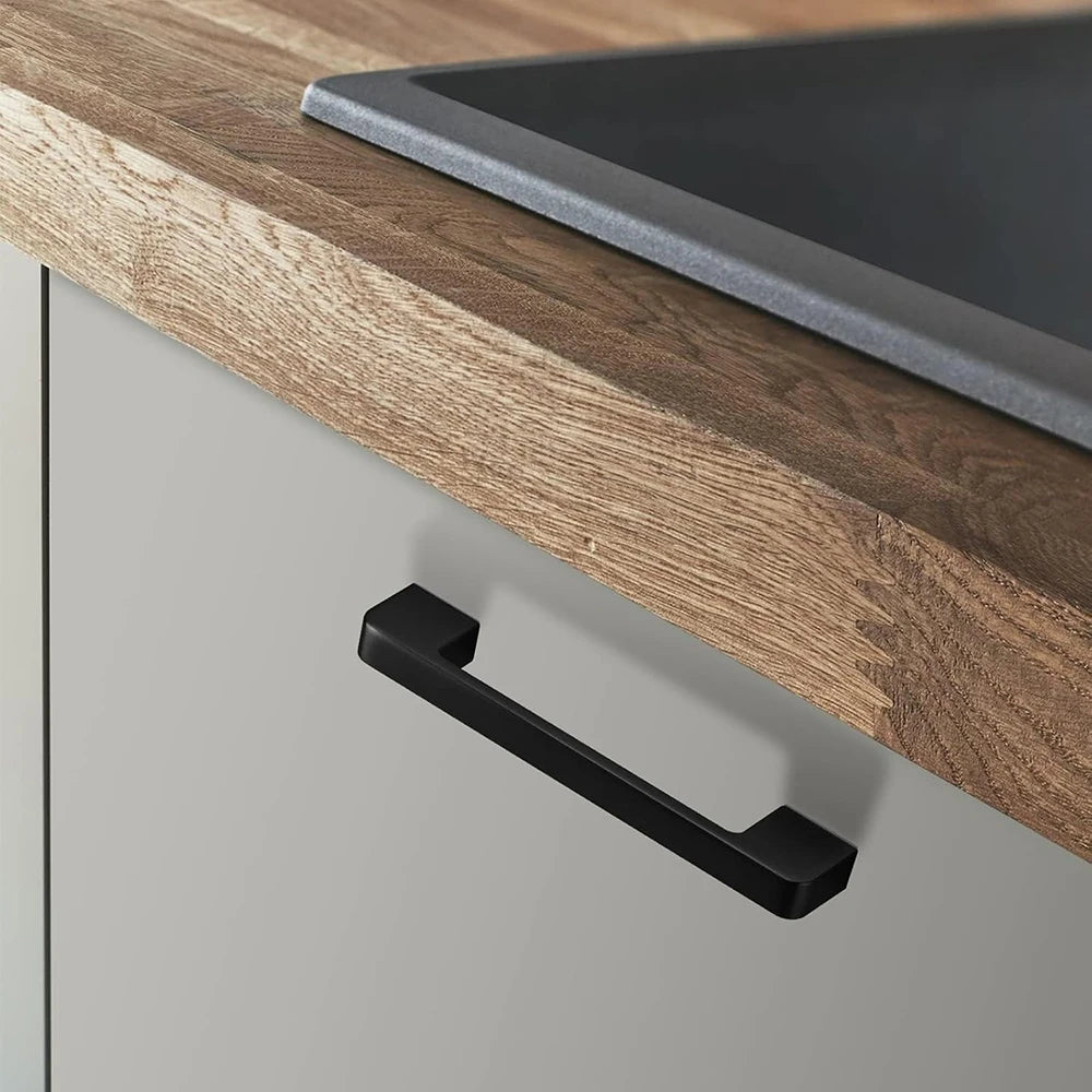 Black kitchen cabinet knob installed on a light gray drawer under a wooden countertop.