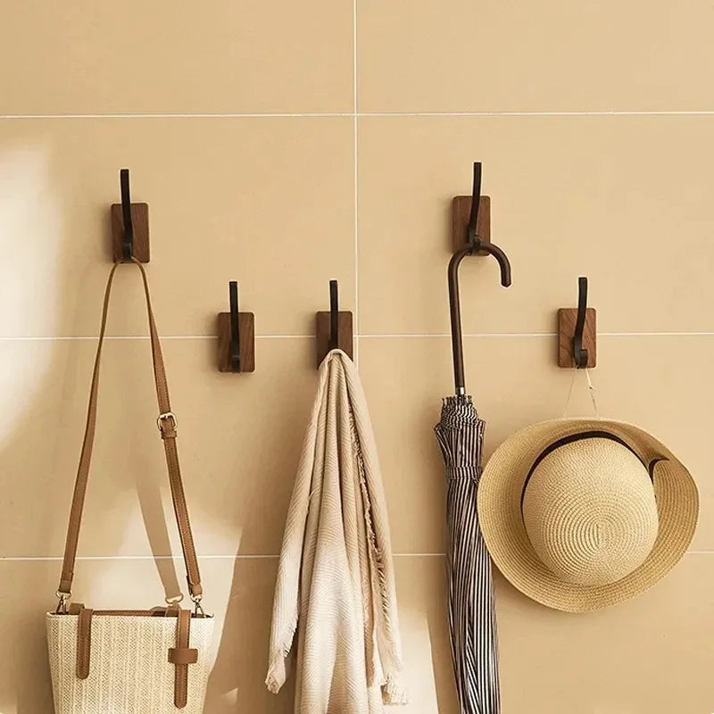 Four wood hooks with black pegs on a tiled wall, holding a bag, a scarf, an umbrella, and a hat.
