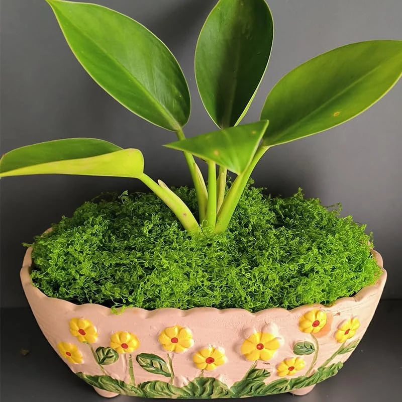 Pink flower pot filled with fake moss and a green plant.