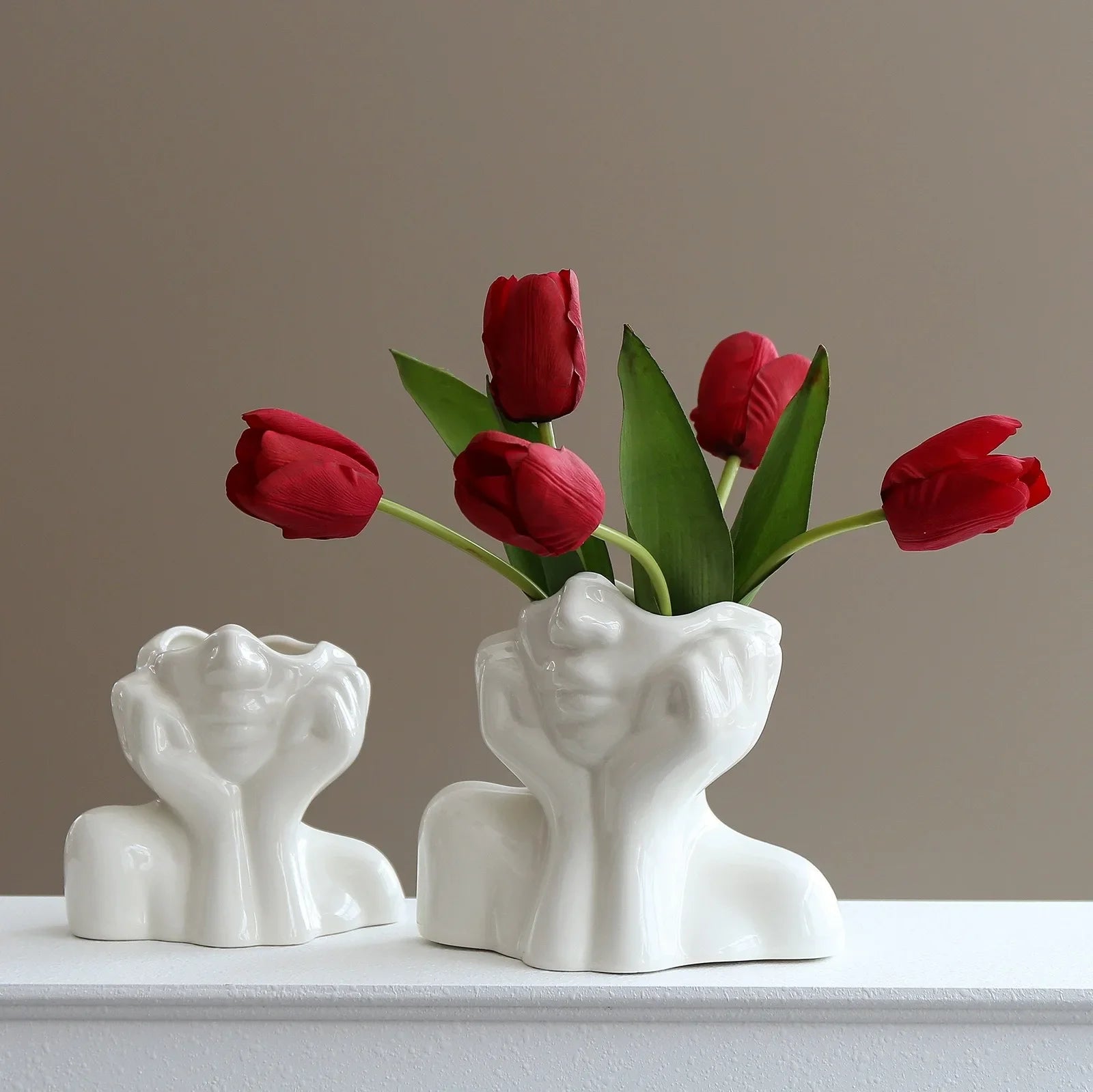 White body shape vase with red tulips displayed in soft light.