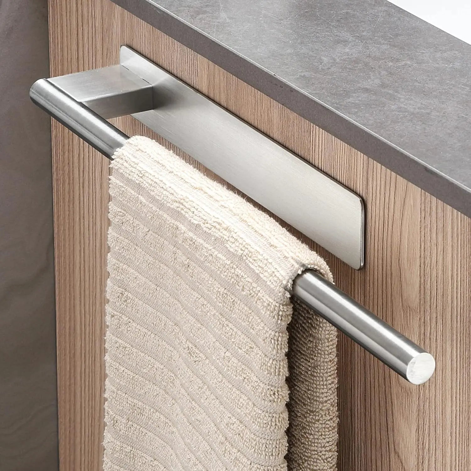 Silver adhesive towel bar mounted on a cabinet door, supporting a beige towel.