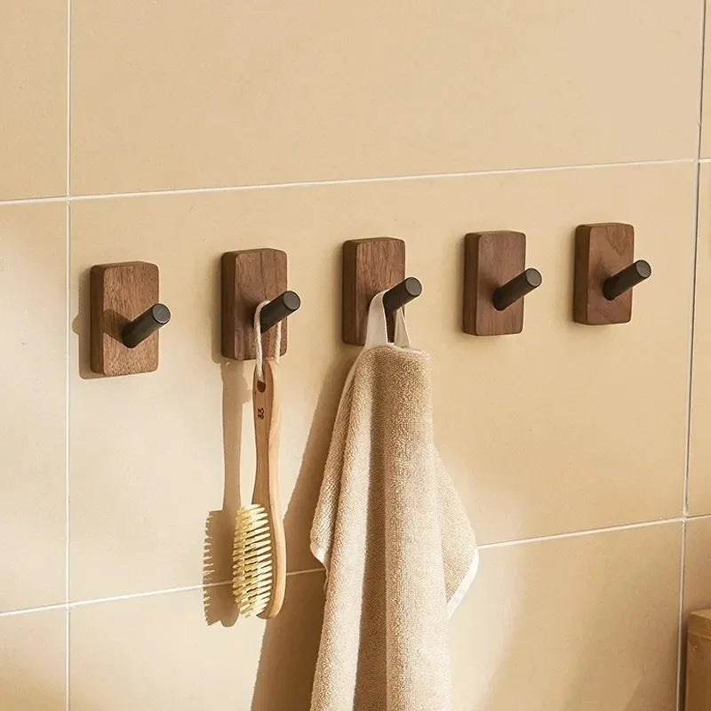 Five wood hooks with short black arms on a tiled wall, holding a towel and brushes.