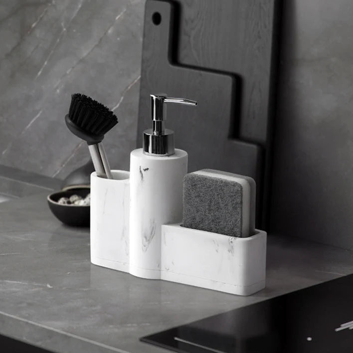 White marble dish soap dispenser with brush and sponge on grey countertop.