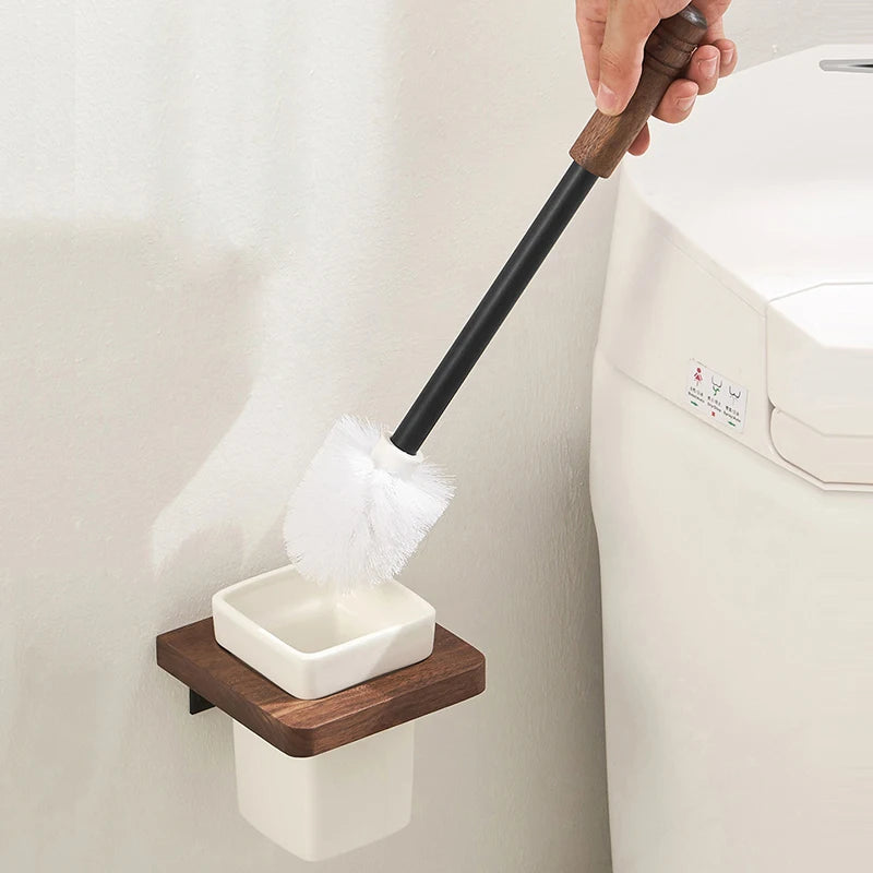 A hand placing a black-handled toilet brush into its wall-mounted wooden holder with a white ceramic base.