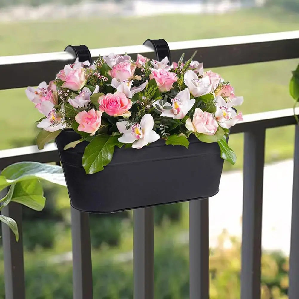 Close-up of black hanging flower pot with pink flowers on fence.