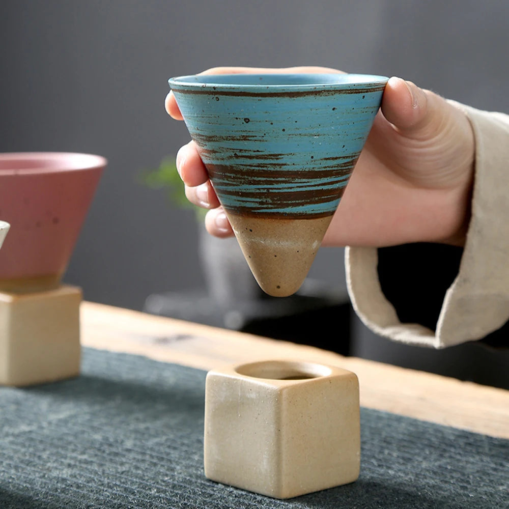 Hand holding a blue textured ceramic coffee cup above a wooden stand.
