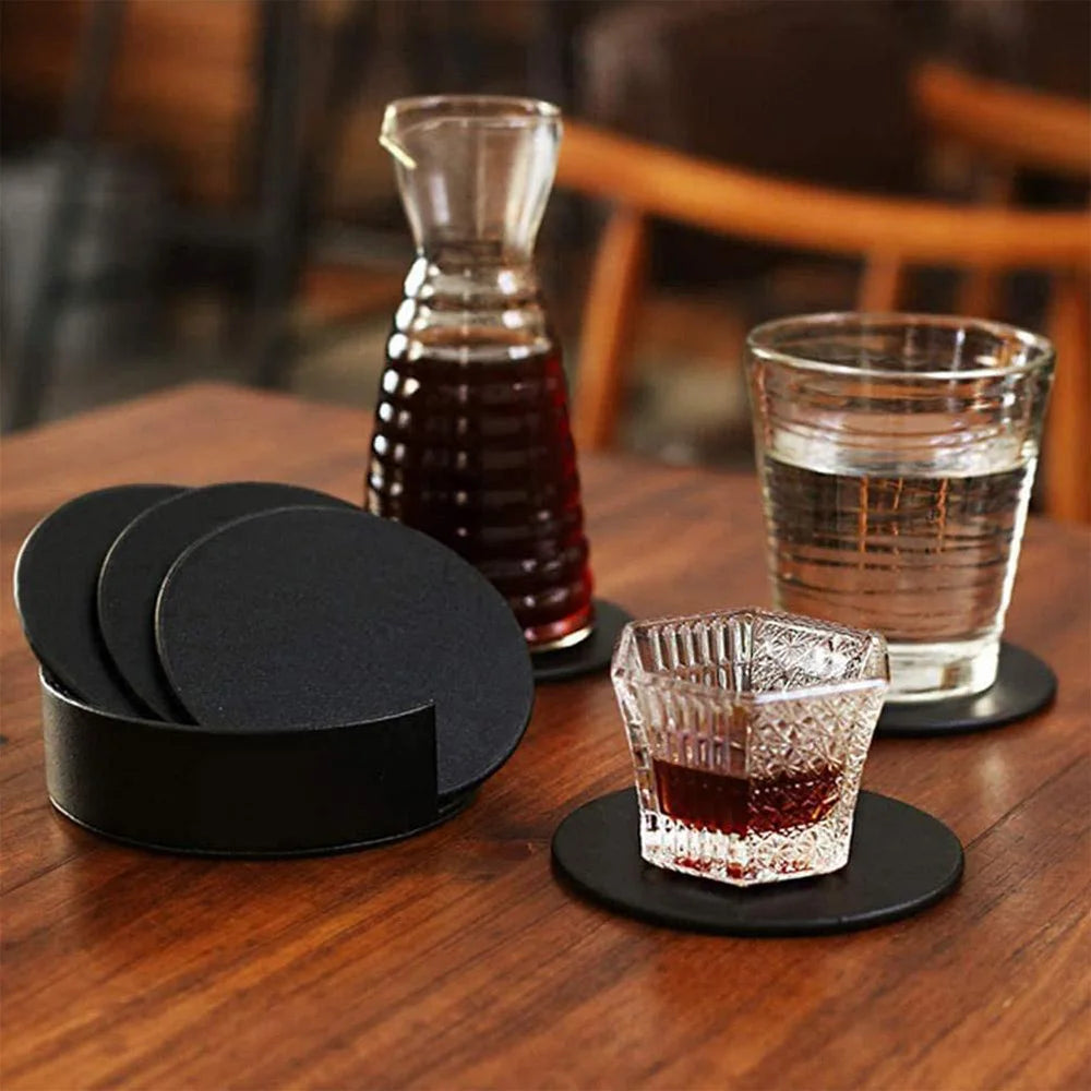 Minimalist black drink coasters on a wooden table, used with water and juice glasses.