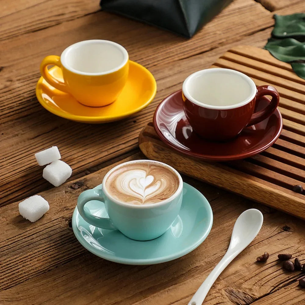Three colorful ceramic mugs and saucers on a wooden table.