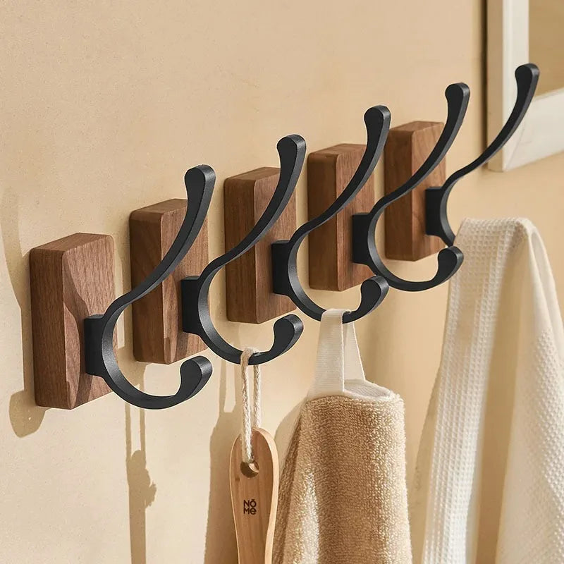 A row of five wood hooks with curved black metal arms, holding towels and a brush.