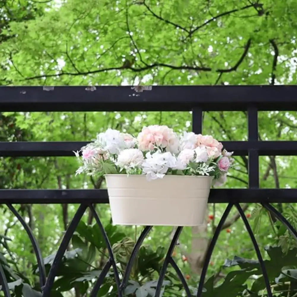 White hanging flower pot with pale pink flowers on a black railing.