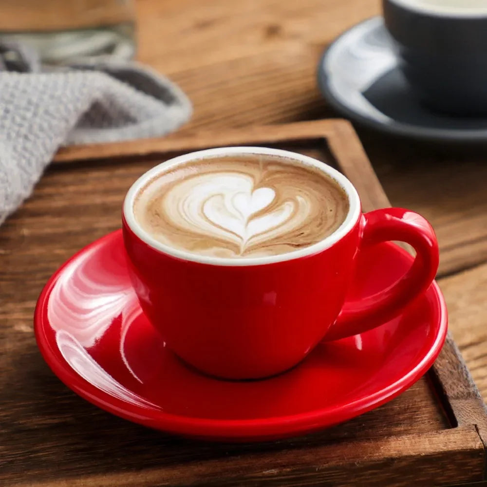 Red ceramic mug with heart latte art on a saucer.